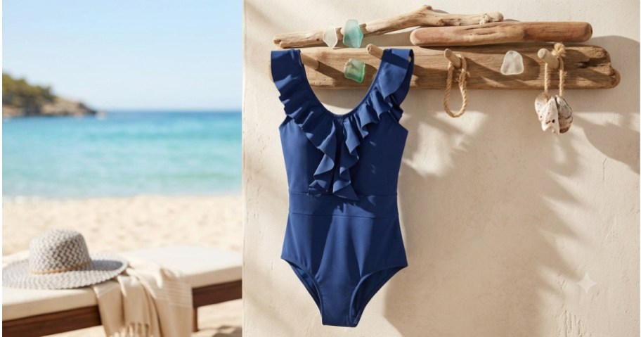 A blue one-piece swimsuit with ruffles hanging on a wooden rack, with a beach and ocean in the background.