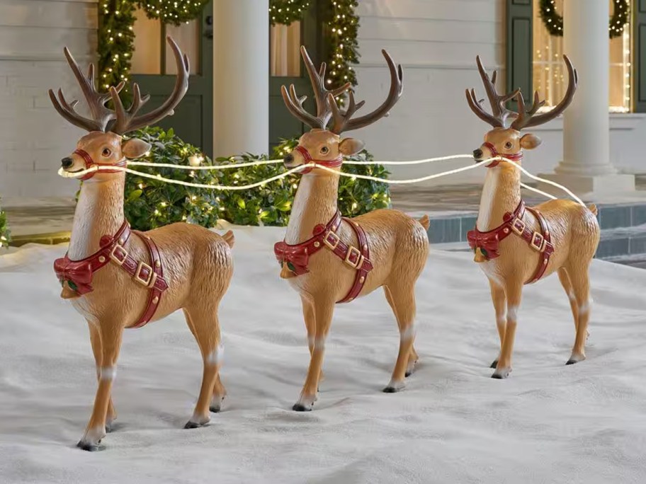 Three lighted Christmas reindeer connected by reins in a snowy yard