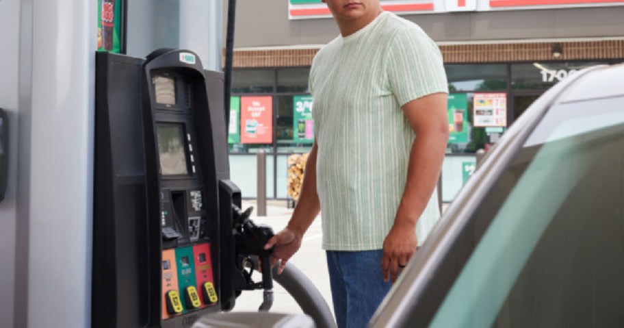 A man standing at a gas pump holding the nozzle next to a car, with a 7-Eleven storefront in the background.