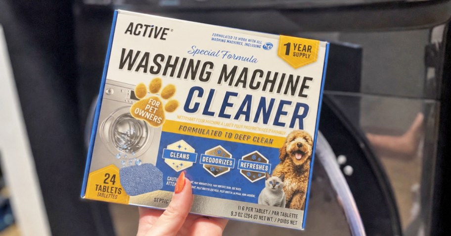 hand holding a box of Active Washing Machine Cleaner in front of washing machine