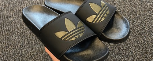 hand holding a pair of black and gold adidas slides