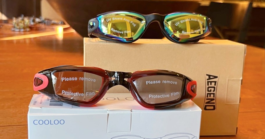 Two pairs of swim goggles, one with mirrored lenses and one with clear lenses, resting on top of their packaging boxes.