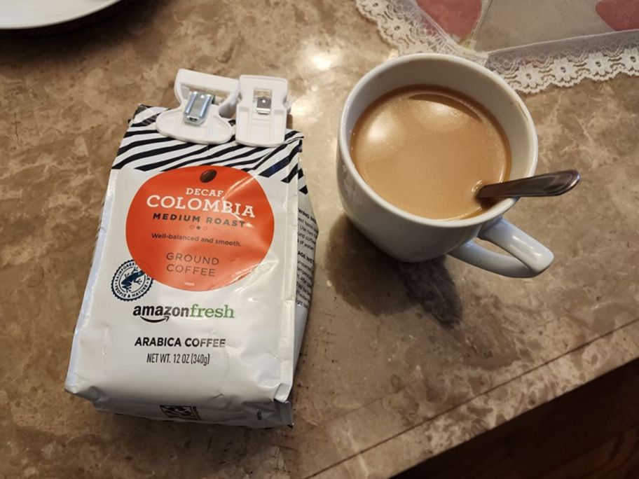 A bag of Amazon Fresh Decaf Coffee next to a mug of coffee with a spoon in it
