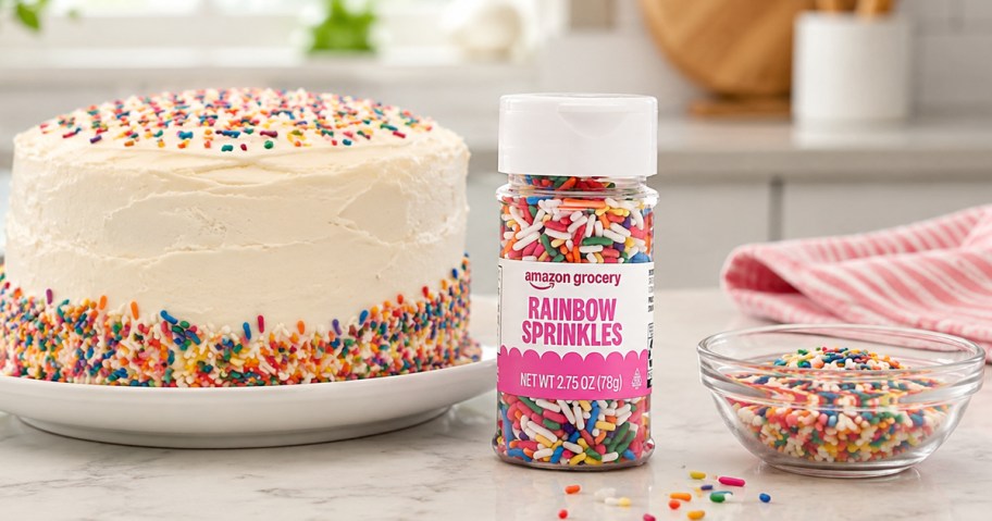 bottle of Amazon Grocery Rainbow Sprinkles on counter near a cake with rainbow sprinkles