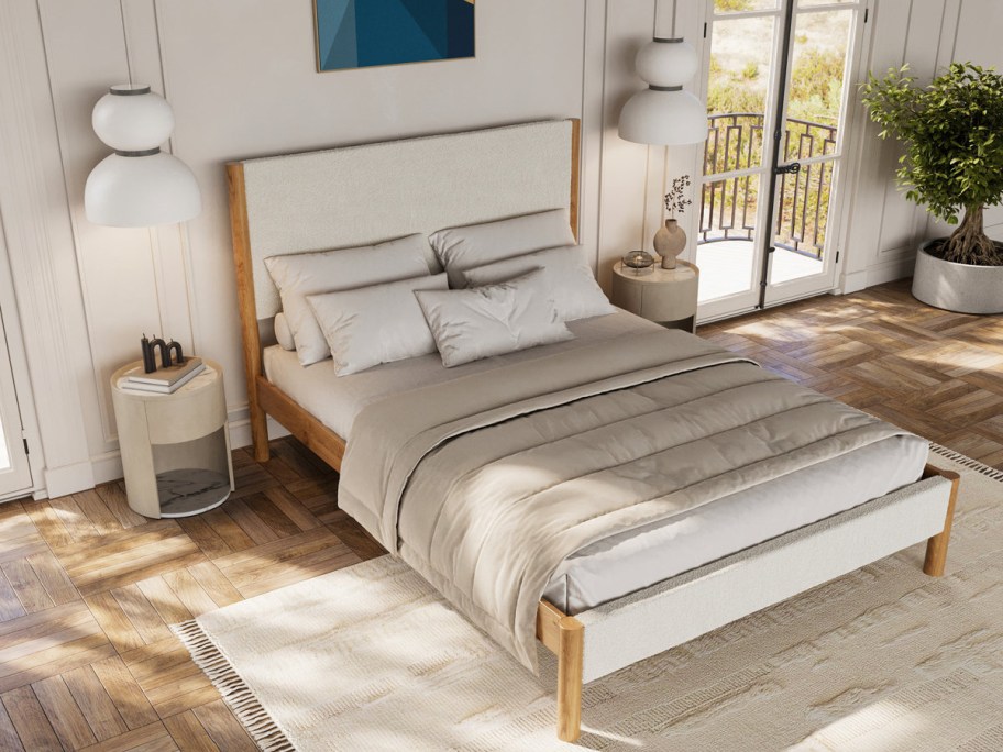 An Ardin solid wood bed frame with a textured white upholstered headboard and footboard, styled with neutral bedding, pillows, and matching round nightstands in a bright bedroom.