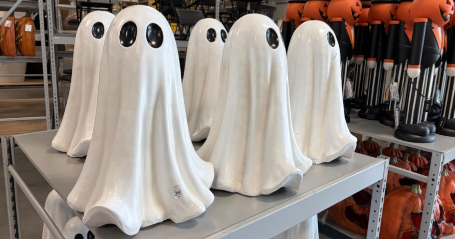 Several white ghost decorations sitting on a store display shelf with other Halloween items in the background.