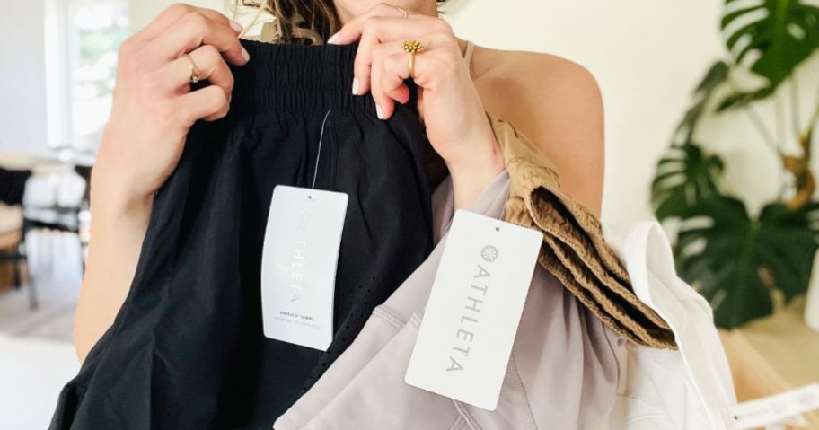 Woman holding several pieces of new athleta clothing with tags on them