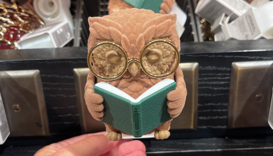 hand holding up a fragrance plug shaped as an owl reading a book