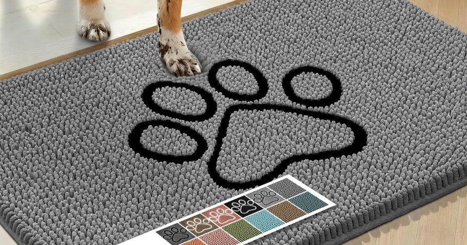 A dog with muddy paws stepping onto a thick grey chenille doormat featuring a large black paw print design in the center.