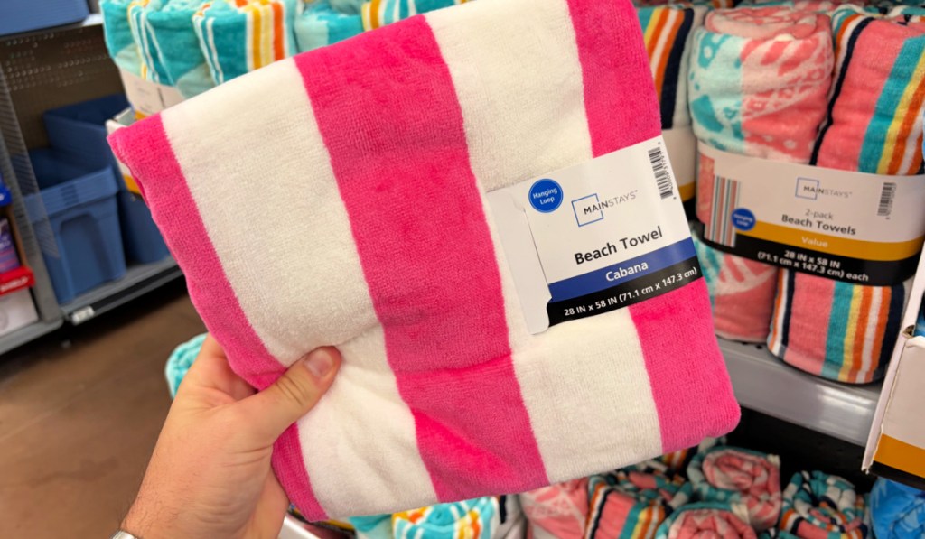 Hand holding up pink and white striped beach towel inside Walmart store
