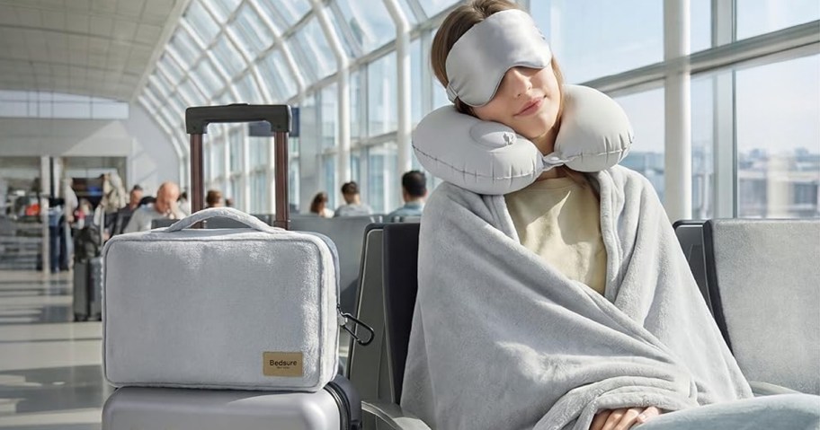 woman sitting at airport with blanket, neck pillow, and eye mask