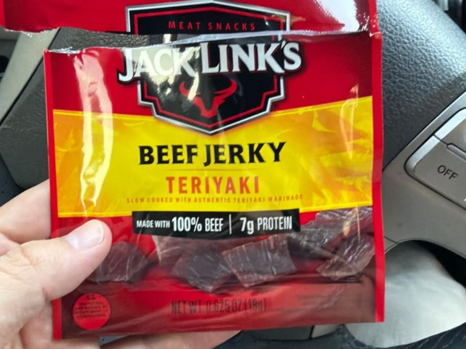 Hand holding Beef Jerky teriyaki package inside of their car