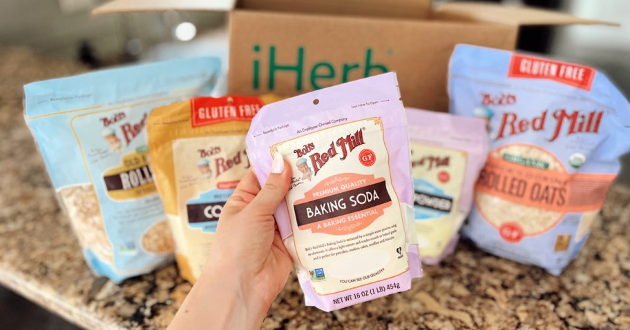 Hand holding Bob's Red mill baking soda in front of other Bob's Red mill products on countertop