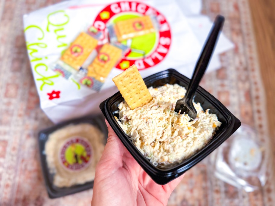hand holding a bowl of chicken salad with a cracker and fork