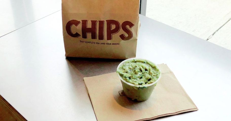 A bag of Chipotle Chips and a plastic ramekin of guacamole on a Chipotle napkin