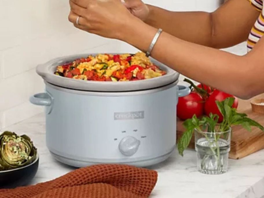woman grating cheese over Crock-Pot Manual Design Series 4.5-Quart Slow Cooker in kitchen