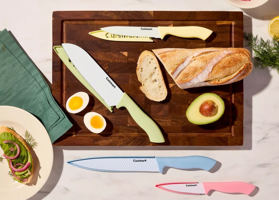 A Cuisinart Advantage 10-piece ceramic color knife set displayed on a wooden cutting board with sliced bread, hard-boiled eggs, avocado, and an avocado toast plate.