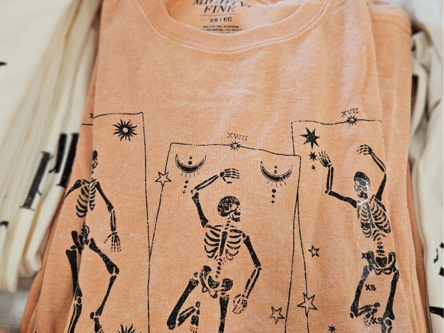 Orange graphic tee with dancing skeletons on it displayed on top of the table