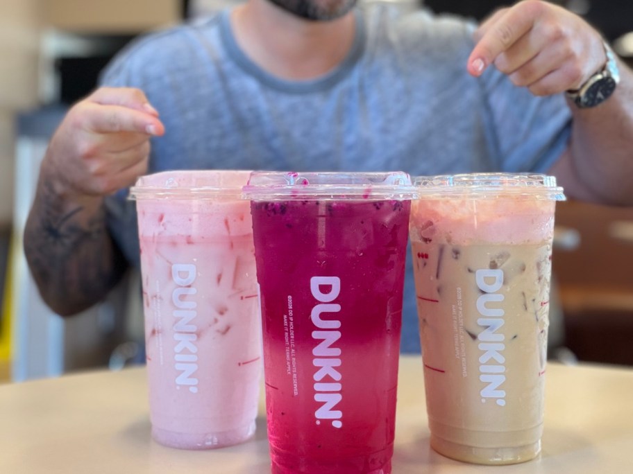 man pointing at 3 different Dunkin drinks