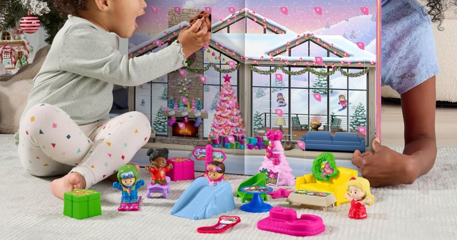 Toddler setting up mini figures and accessories in front of the fold-out Barbie ski chalet calendar