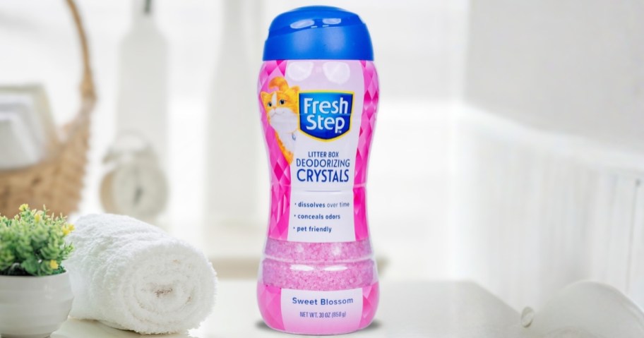 bottle of fresh step cat litter deodorizing crystals on bathroom counter with towel and plant