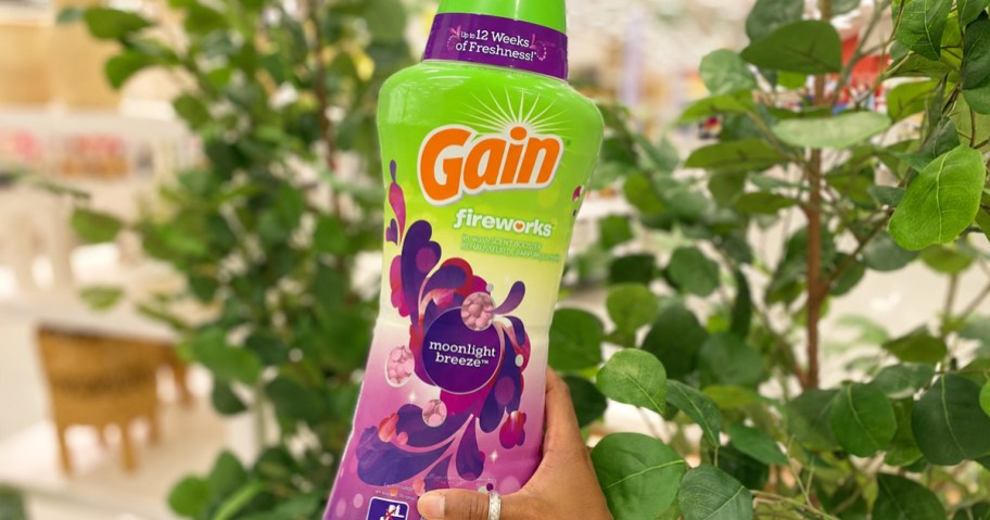 hand holding up a bottle of Gain Laundry Scent Booster Beads near green leaves