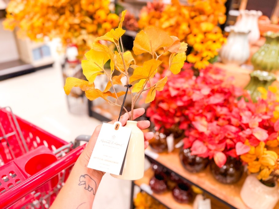 holding a small white vase with yellow gingko stems in it