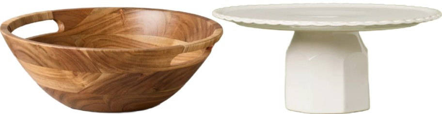 A large wooden serving bowl with cutout handles next to a white ceramic cake stand against a plain white background.