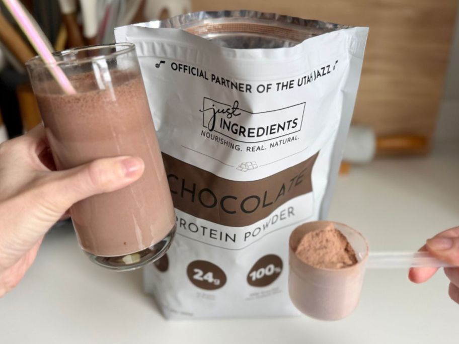 Just Ingredients A bag of chocolate protein powder, one scoop of powder and a glass of brown liquid in front of it.