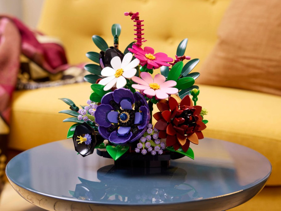 A LEGO botanical flower arrangement featuring colorful blooms and green leaves sitting on a round table.