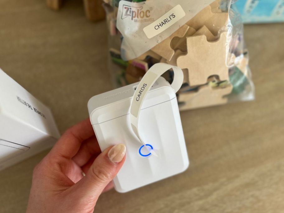 Hand holding a small wireless label maker with a label printed a bag of puzzle pieces with a label behind it