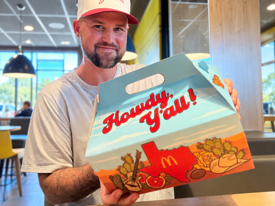 Smiling man holding a McDonald’s Texas Meal box inside a restaurant.