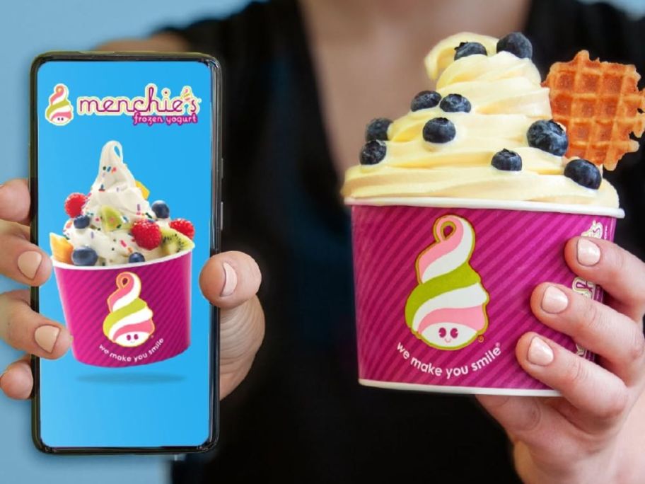 Woman holding a cell phone with Menchi app and a glass of frozen yogurt