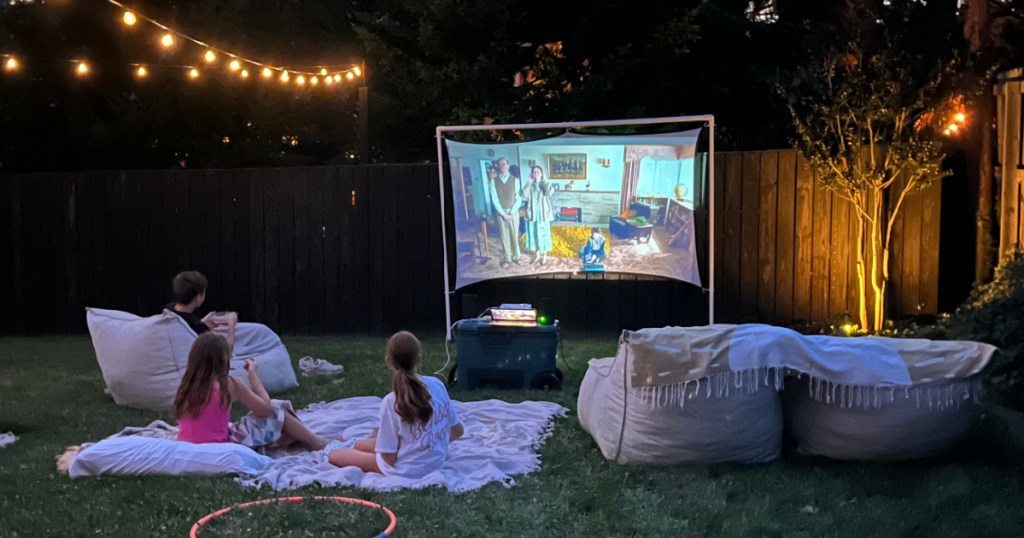 Family watching movie outside on screen using mini projector