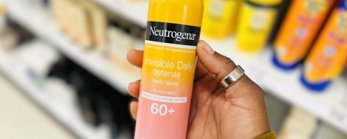 hand holding a pink and orange bottle of Neutrogena Invisible Daily Defense Sunscreen Spray