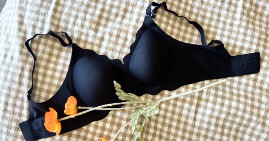 A black scalloped jelly bra laying on a bed with flowers