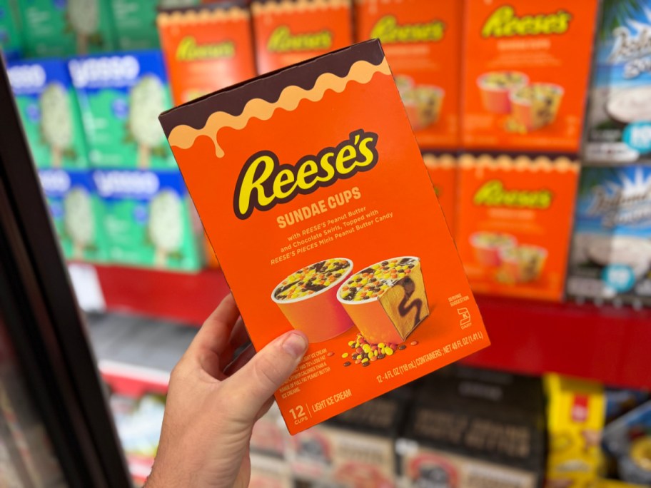 A box of Reese's Sundae Cups light ice cream being held in front of a store freezer display.