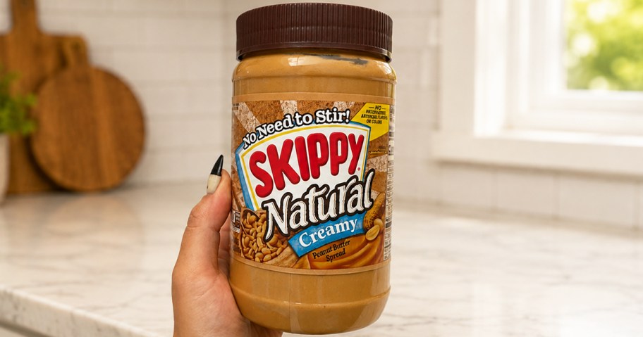 hand holding up a jar of Skippy Natural Creamy Peanut Butter in kitchen