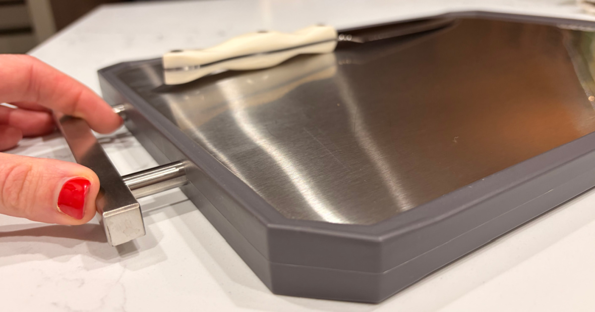 Hand holding stainless steel cutting board on white kitchen countertop