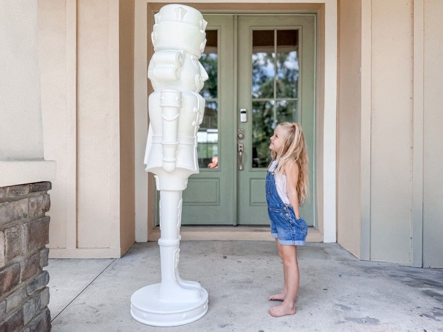 Girl standing in front of a huge white nutcracker on the front porch