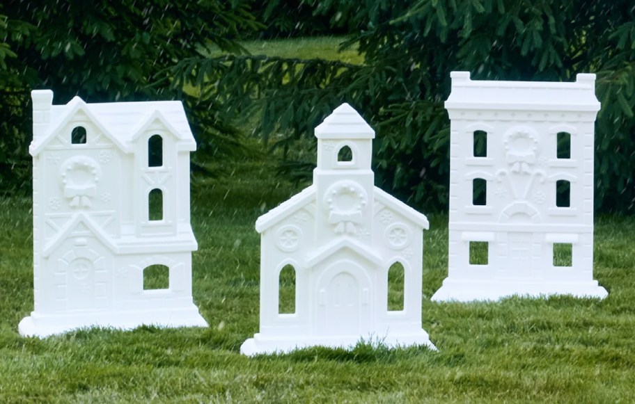 Three large white plastic Christmas village decoration pieces on the grass