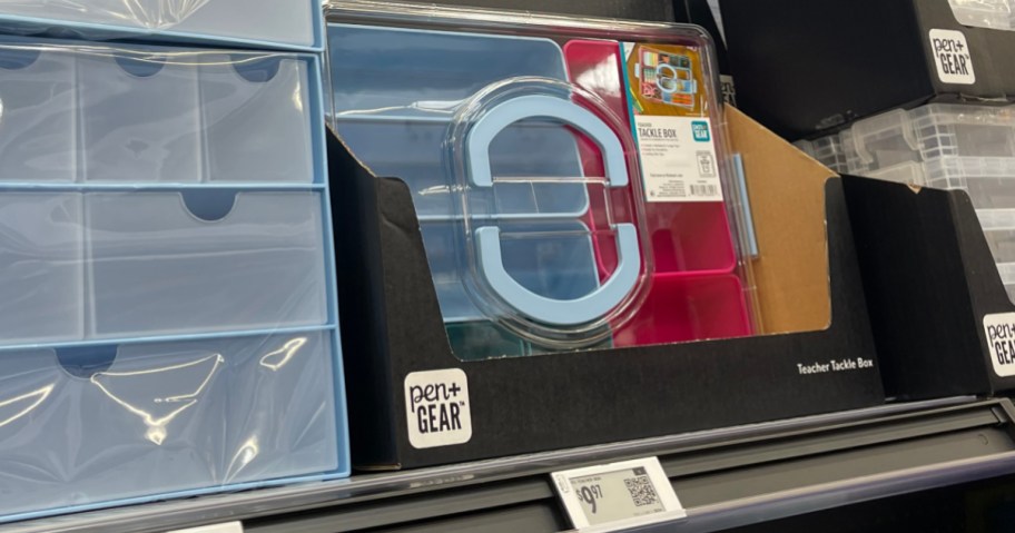 A clear plastic Pen+Gear Teacher Tackle Box with a light blue handle and blue and pink compartments sitting on a store shelf.