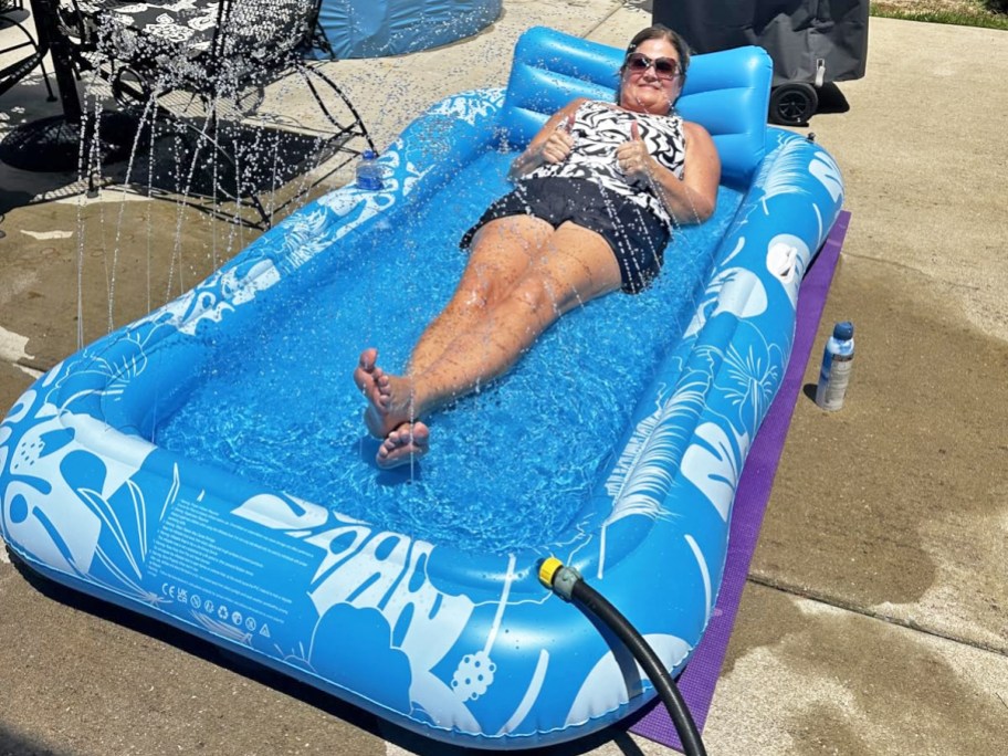 woman laying in a blue inflatable pool with sprinklers