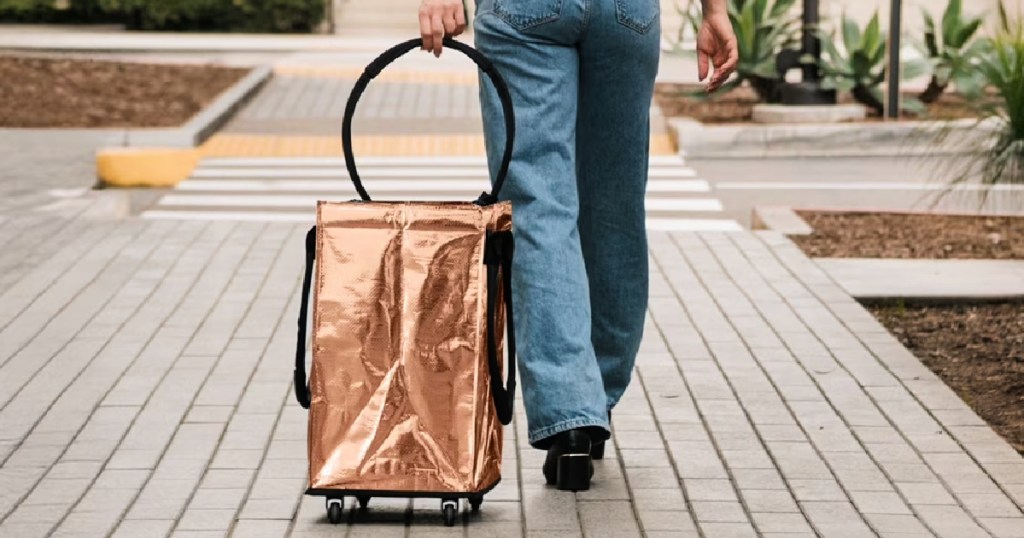 Women holding gold colored, rolling tote while walking outside
