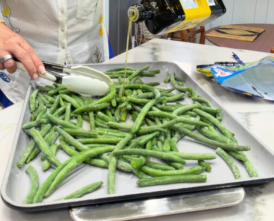 adding olive oil to frozen green beans on a sheet pan