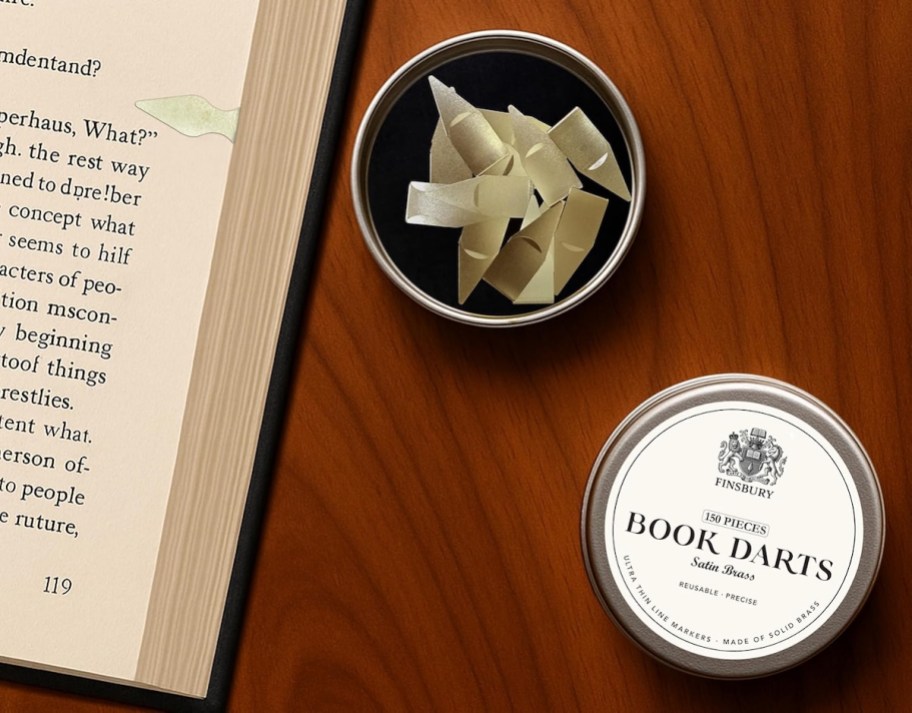Dish of brass book darts sitting on wood table next to book