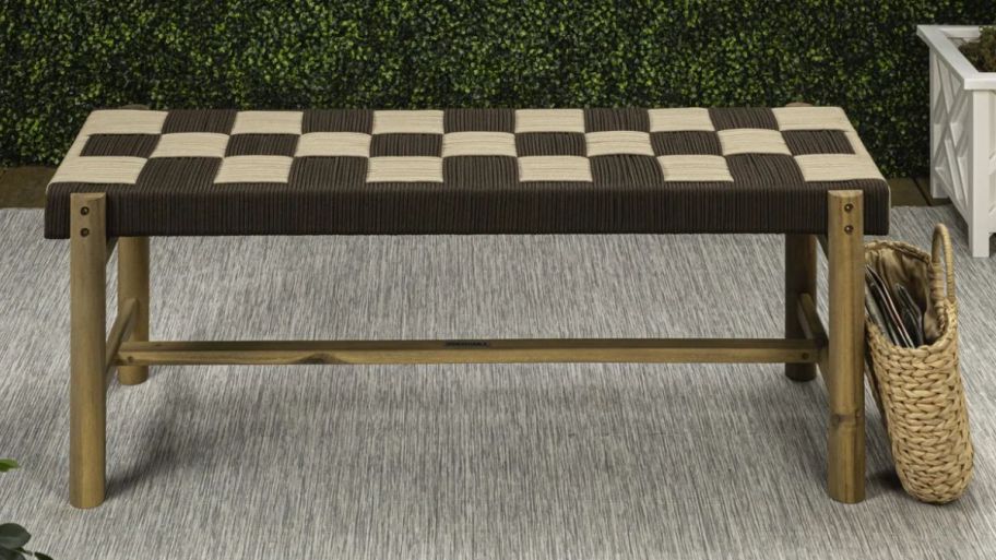 Checkered bench outside next to a wicker basket on a rug