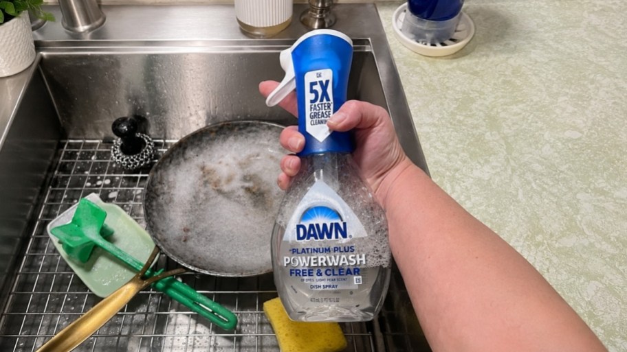 womans hand holding a bottle of dawn power wash spray at a kitchen sink