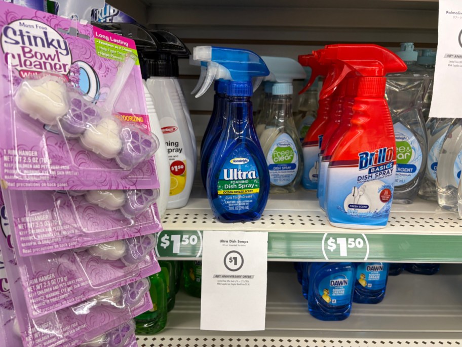 A store shelf displaying various cleaning supplies, including hanging toilet bowl cleaners and bottles of dish spray, with a hanging paper sign advertising a $1 sale price.