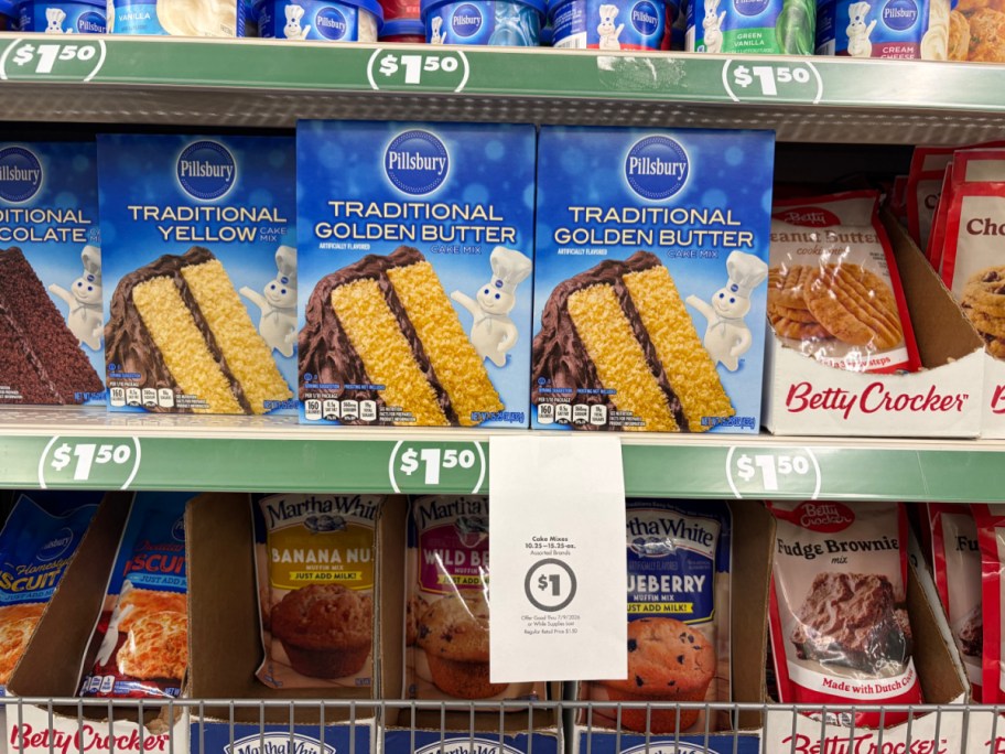A store shelf displaying boxes of Pillsbury cake mix with a hanging paper sign advertising a $1 sale price.